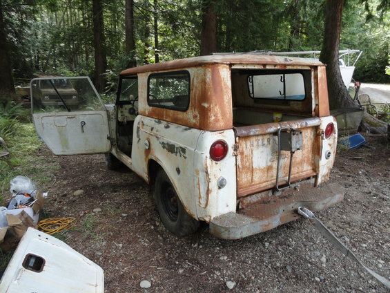 Rusted white International Scout with doors open, parked in a wooded area