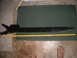 1992 Ford Bronco - A black metal automotive part is measured with a yellow tape measure on a dark green mat.