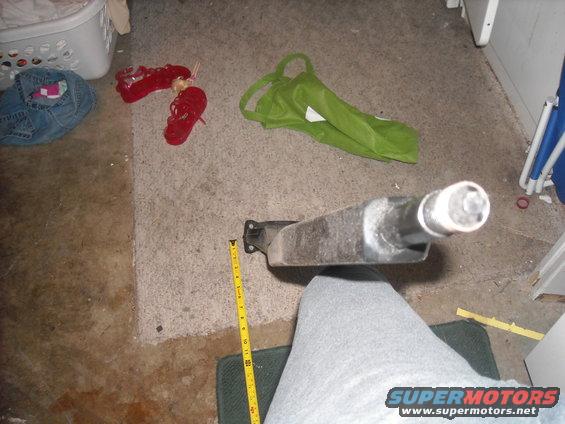 Vehicle suspension part being measured with a yellow tape measure on a carpeted floor