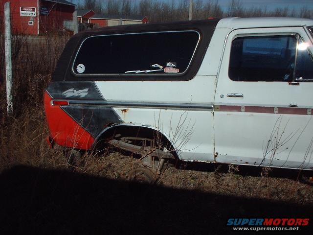 Side view of a white and red Ford Bronco with a black top, parked in tall grass