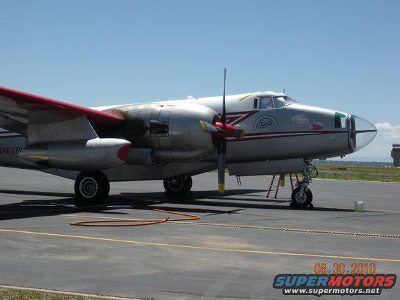 Twin-engine airplane with red-tipped wings parked on an airport tarmac. Serial number 496279 is visible on the fuselage