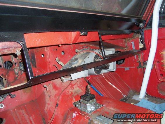 Vehicle interior showing dashboard removed, exposed red metal, and a shifter assembly