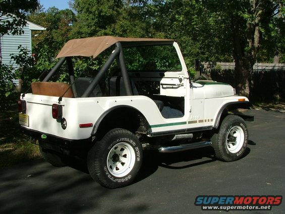 White Jeep CJ5 with brown soft top and green stripe, parked on asphalt driveway