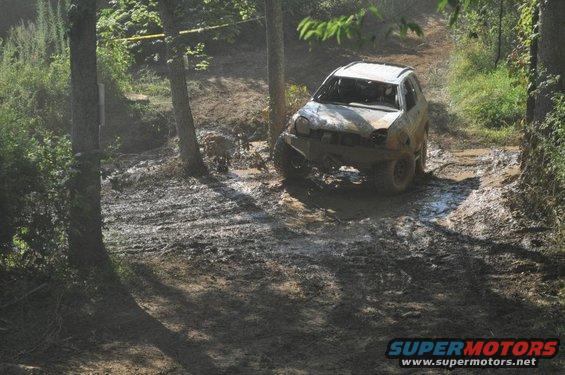 Muddy off-road vehicle navigating a dirt track with trees and mud