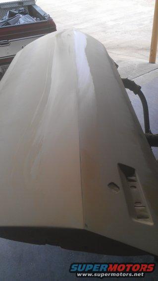 Car hood covered in primer and filler, with a portion of a pickup truck bed visible in the background