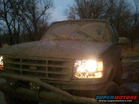 1993 Ford Bronco covered in mud, headlights on