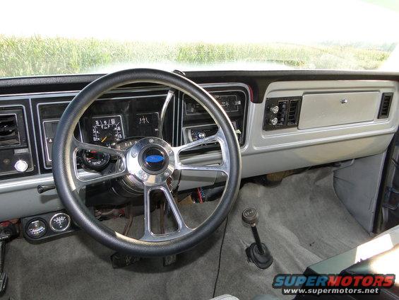 Interior shot of a truck's dashboard with a custom steering wheel and floor shifter. Gauges are visible