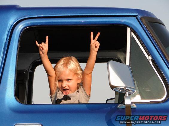 Blue 1978 Ford Bronco side view with a child in the window making rock on and peace signs