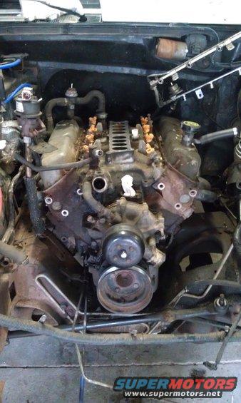 Engine bay with fuel injectors and intake manifold visible. Some hoses and belts are disconnected