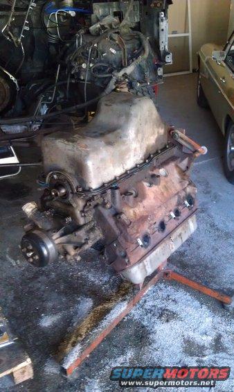 Engine on an orange stand, with a partial vehicle frame behind it