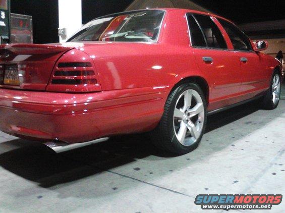 Red sedan with a spoiler and custom wheels parked at a gas station