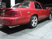 Red 1999 Ford Crown Victoria parked, showing rear quarter panel and custom wheels