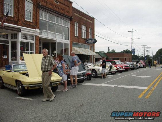 Yellow convertible with hood open, parked on street with other classic cars