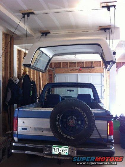 Rear view of a 1988 Ford Bronco with its top removed and hoisted above it in a garage