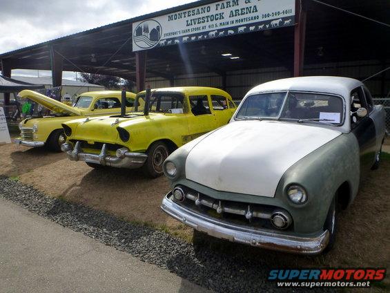 Front of a light-colored classic car, with two yellow cars behind it