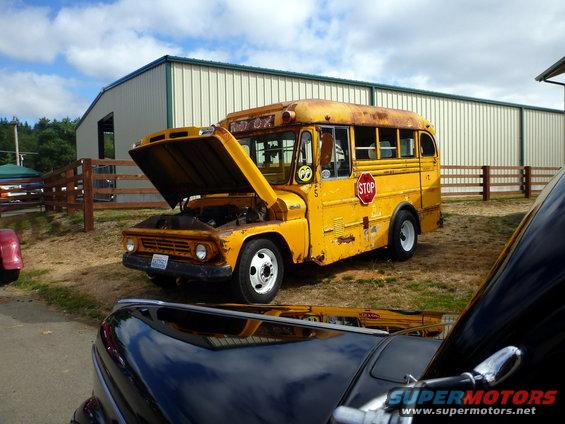 Yellow school bus with hood open, parked outside a building