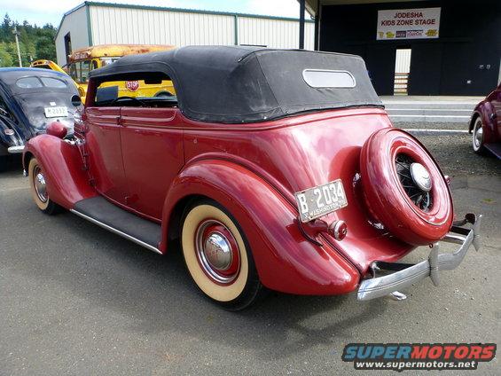 Red convertible with a black top and a spare tire mounted on the rear. Whitewall tires are visible