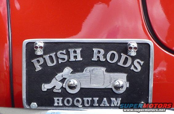 Close-up of a red surface with a black license plate that says 'POSH RODS HOOTAN' and has a silhouette of a car