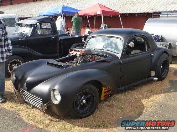 Black custom hot rod coupe with flames on the fender, exposed engine with a scoop, and chrome grille