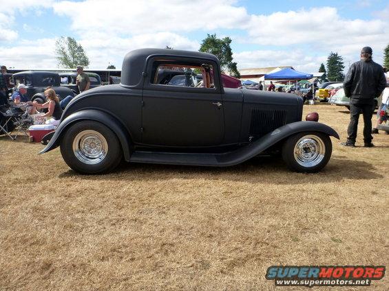 Black hot rod coupe with chrome wheels parked on dry grass
