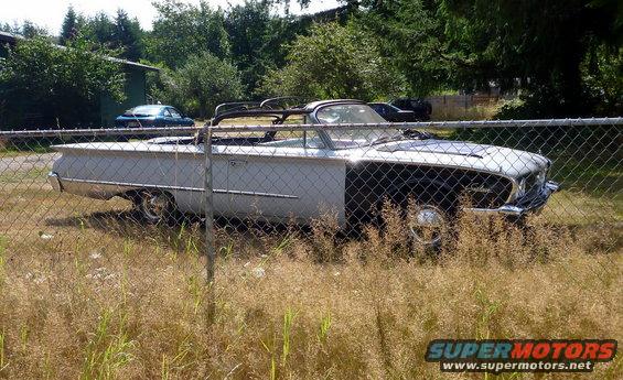 White convertible automobile with a black front end, seen through a chain-link fence