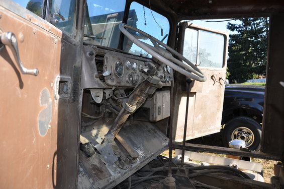 Interior of a brown truck cab showing dashboard and steering wheel. Another vehicle is visible through the open door