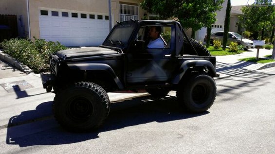 1987 Suzuki Samurai with large off-road tires and custom paint, driving on a suburban street