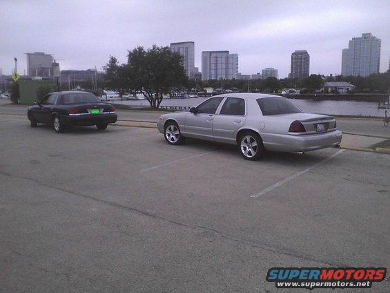 Silver 2003 Ford Crown Victoria parked in a lot, 3q-front view, with a black car behind it