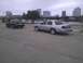 2003 Ford Crown Victoria - Two Ford Crown Victorias are parked in a lot near a body of water with city buildings in the background.