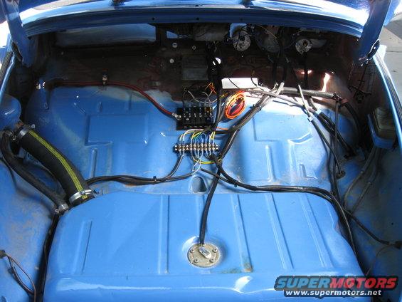 Blue car interior with exposed wiring, fuel tank, and fuse box