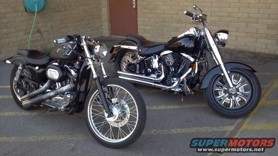 Two black Harley-Davidson motorcycles parked side-by-side in front of a brick wall