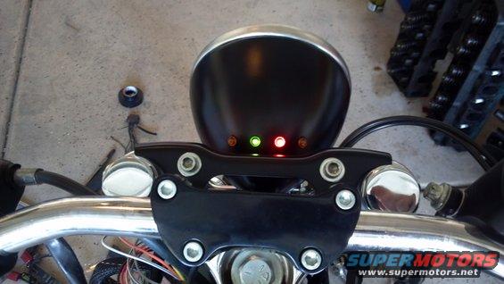 Motorcycle handlebars with a black headlight housing and three indicator lights (two red, one green)
