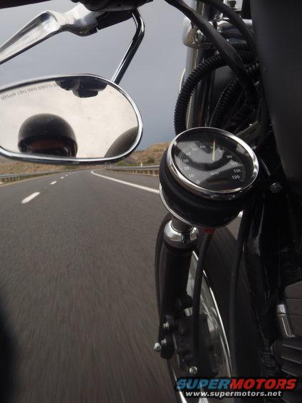 Motorcycle speedometer on a highway, rider reflected in mirror