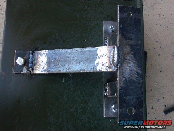 Close-up of a welded metal bracket attached to a dark green surface