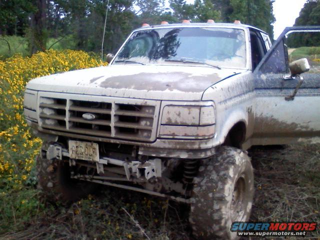 Mud-covered pickup truck with lifted suspension and large tires, front view