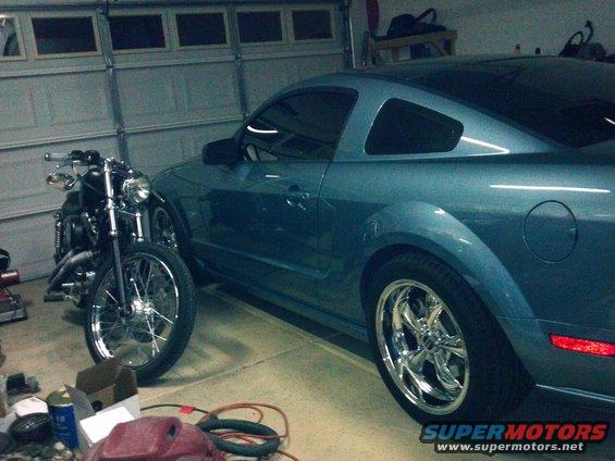 Blue coupe parked next to a motorcycle in a garage