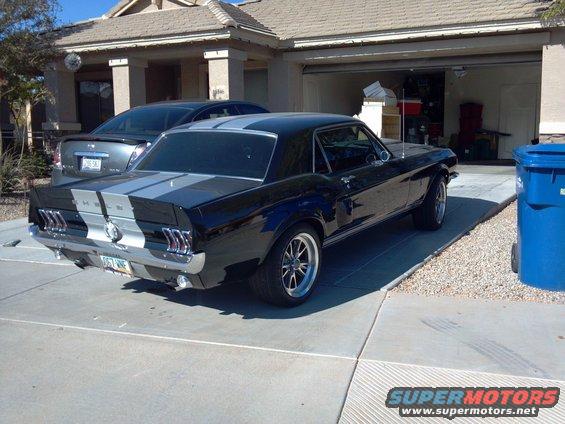 Black 1967-1968 Ford Mustang with silver racing stripes, parked in a driveway