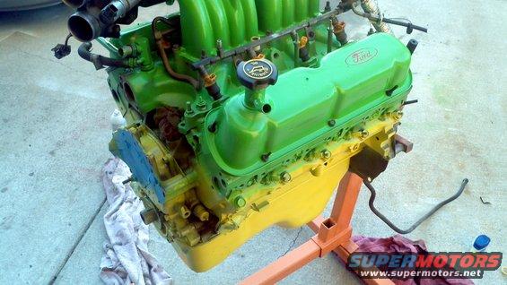 Green and yellow Ford V8 engine on an orange stand, with "Ford" logo visible on the valve cover