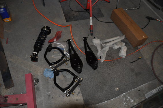 Car suspension parts laid out on a garage floor, including a coilover shock and control arms