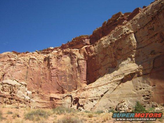 Red rock formations under a clear blue sky with desert vegetation in the foreground
