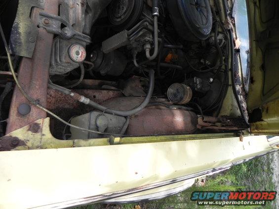 Yellow vehicle engine bay with visible rust and hoses
