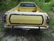 1974 Ford Ranchero - The rear of a yellow pickup truck with a chrome bumper and a tow hitch is shown in an outdoor setting.