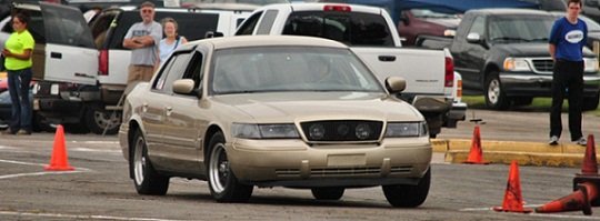 Gold sedan, front view, in a parking lot with cones