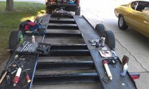 Car trailer with tools laid out, a yellow car on the right, and a truck in the background