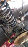 Rusty coil spring and suspension parts on a red jack, with a brake rotor visible