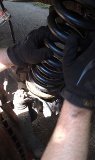 Hands in black gloves working on a vehicle's suspension spring and shock
