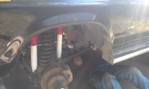 Person working on rear axle with new red and white shocks installed