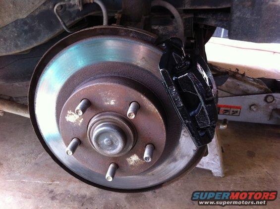 Car brake rotor with rust and blueing, black caliper, on jack stand
