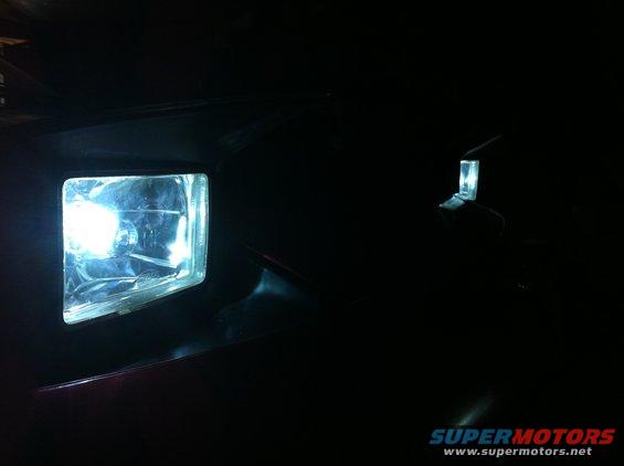 Close-up of a vehicle's illuminated headlight and a distant side marker light
