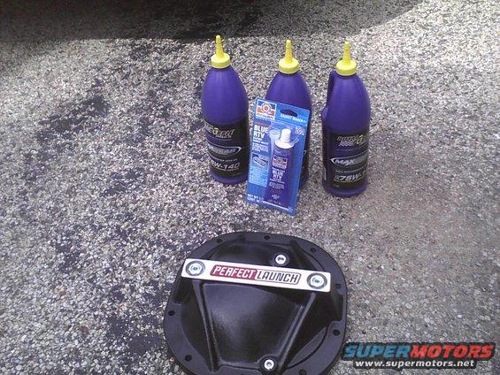 Black differential cover with "PERFECT LAUNCH" label, three bottles of gear oil, and a tube of RTV sealant on asphalt